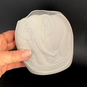 May include: White ceramic elephant planter with a textured surface. The elephant is standing in a water design.