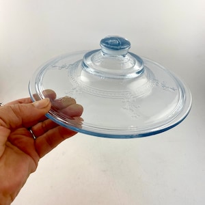 May include: A light blue glass lid with a raised center and a decorative pattern around the edge.