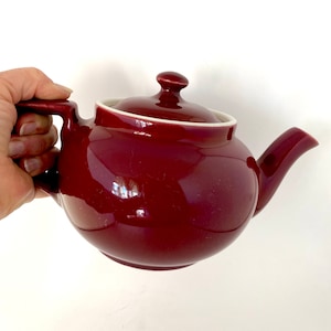 May include: A burgundy ceramic teapot with a white lid and handle.