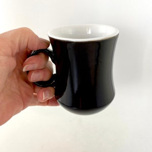 May include: A black ceramic coffee mug with a white interior and a rounded handle.