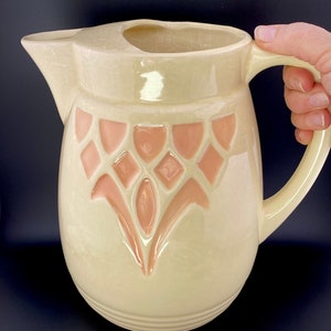 May include: A cream-coloured ceramic jug with a pink floral design. The jug has a wide mouth and a handle.