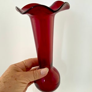 May include: A deep red glass vase with a ruffled top and a round base. The vase is clear at the bottom.
