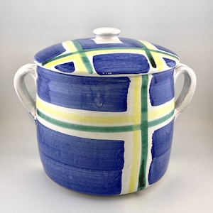 May include: A blue and white ceramic jar with a lid. The jar features a geometric pattern of yellow, green, and blue stripes. The lid has a white knob.