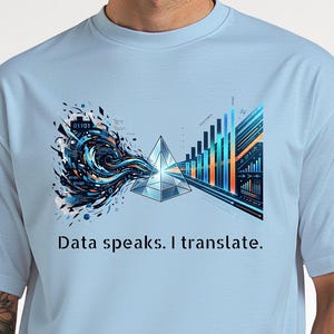 May include: Pale blue t-shirt with a graphic design. The design includes a geometric crystal and data visualization elements in blue, orange, and white. The text "Data speaks. I translate." is printed below.