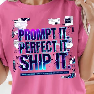 Könnte beinhalten: Ein leuchtend pinkfarbenes Kurzarm-T-Shirt mit einem Grafikdruck, der den Text PROMPT IT. PERFECT IT. SHIP IT. in einer blau-violetten Glitch-Schrift zeigt, umgeben von kleinen digitalen Datenboxen und technischen Textelementen.