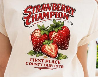 Puede incluir: Una camiseta de manga corta color crema con un gráfico de tres fresas y el texto "STRAWBERRY CHAMPION" arriba y "FIRST PLACE COUNTY FAIR 1978" abajo. La camiseta se combina con unos pantalones cortos de mezclilla azul claro con botón.