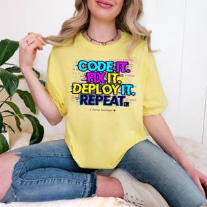 Cornsilk tee with a colorful vibrant glitch-style programming quote. "Code Fix Deploy Repeat" graduation gift for Class of 2026 computer science majors.