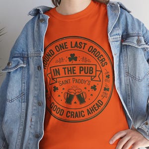 Orange unisex t-shirt featuring the "Good Craic Ahead" pub seal design in dark green. A fun, playful twist on traditional St. Patrick's Day gear, perfect for women or men who want a softer color palette while keeping the Irish drinking humor.