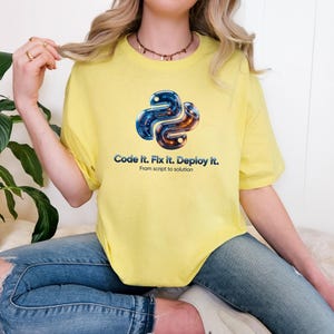 Cornsilk t-shirt featuring a futuristic 3D metallic python snake with glowing internal code. Text: "Code it. Fix it. Deploy it." Modern tech gift for 2026 software engineers.