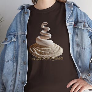 K&ouml;nnte beinhalten: Dunkelbraunes T-Shirt mit einem wei&szlig;en Schlangenmuster, das sich auf einer strukturierten, beigefarbenen Basis windet. Der Text "The Zen of Python" ist in Hellbraun gedruckt. Die Person tr&auml;gt eine Jeansjacke.