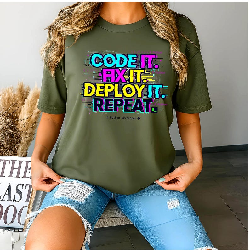 Military green t-shirt with electric neon cyan and magenta glitch text. High-contrast "Code It Fix It" design for Python developers and computer science students. Edgy hacker aesthetic.