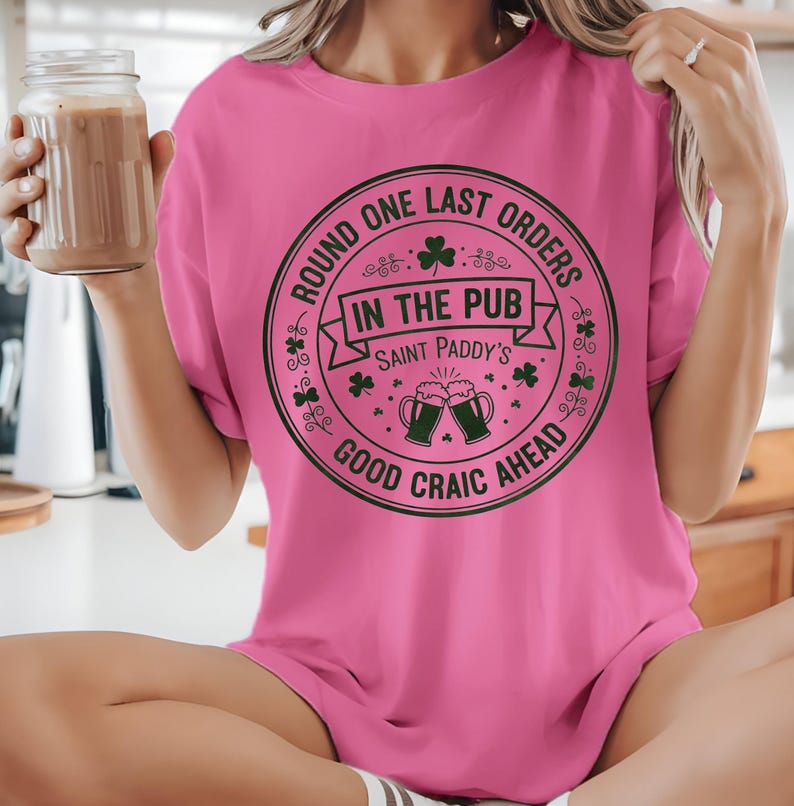 Azalea pink unisex t-shirt featuring the "Good Craic Ahead" pub seal design in dark green. A fun, playful twist on traditional St. Patrick's Day gear, perfect for women or men who want a softer color palette while keeping the Irish drinking humor.