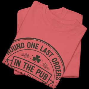 Coral Silk unisex t-shirt featuring the "Good Craic Ahead" pub seal design in dark green. A fun, playful twist on traditional St. Patrick's Day gear, perfect for women or men who want a softer color palette while keeping the Irish drinking humor.