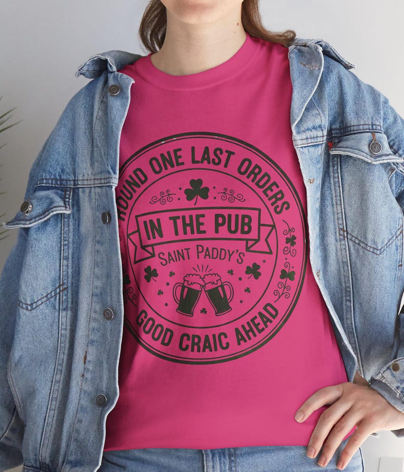 Heliconia pink unisex t-shirt featuring the "Good Craic Ahead" pub seal design in dark green. A fun, playful twist on traditional St. Patrick's Day gear, perfect for women or men who want a softer color palette while keeping the Irish drinking humor.