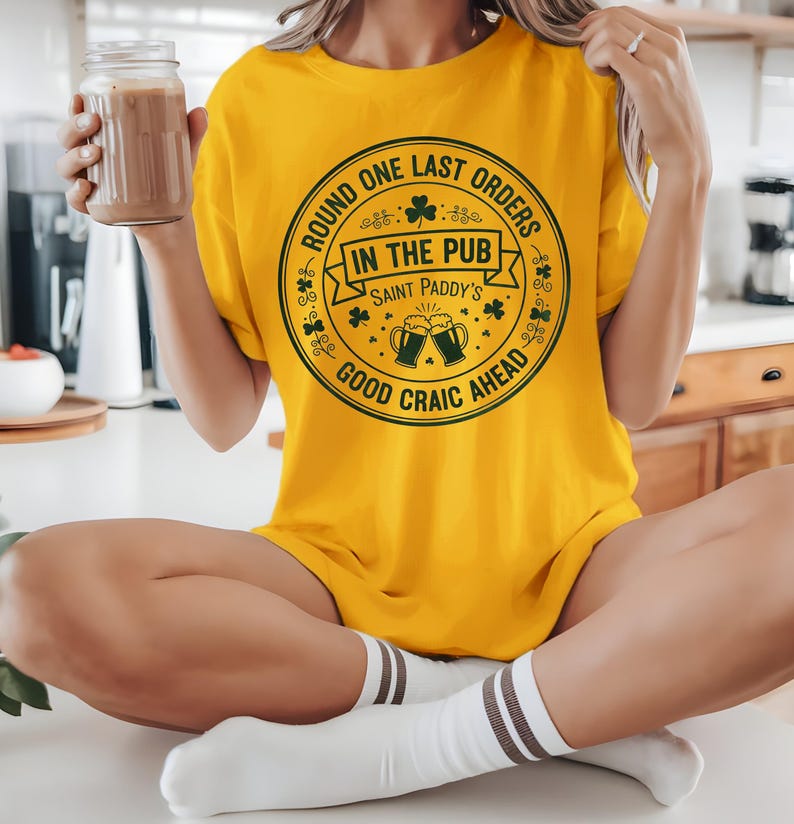 Gold unisex t-shirt with a dark green "Last Orders In The Pub" emblem. The vintage-style beer mug graphic and shamrock details give it a retro, worn-in Irish bar feel, ideal for a casual, understated St. Patrick's Day outfit.