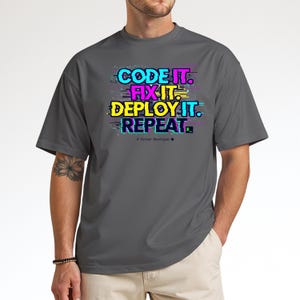 Charcoal grey t-shirt with a neon glitch typography design: "CODE IT. FIX IT. DEPLOY IT. REPEAT." and "# Python Developer". Gritty, modern streetwear for programmers and engineers.
