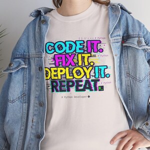 Ice grey t-shirt with a neon glitch typography design: "CODE IT. FIX IT. DEPLOY IT. REPEAT." and "# Python Developer". Gritty, modern streetwear for programmers and engineers.