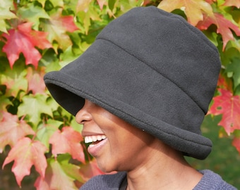 May include: A person wearing a black fleece bucket hat with a wide brim. The hat is worn low on the forehead and the person is smiling.