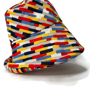 May include: A bucket hat with a colorful geometric pattern in shades of red, yellow, blue, black, and gray. The pattern is made up of horizontal stripes of different widths.