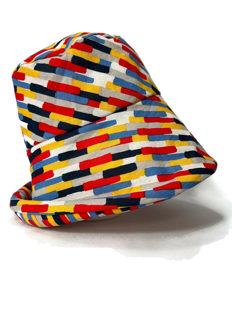 May include: A bucket hat with a colorful geometric pattern in shades of red, yellow, blue, black, and gray. The pattern is made up of horizontal stripes of different widths.
