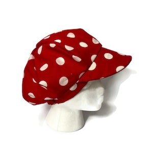 Peut inclure: Casquette de newsboy à pois rouge et blanc avec une visière. La casquette est en tissu et a un style classique.