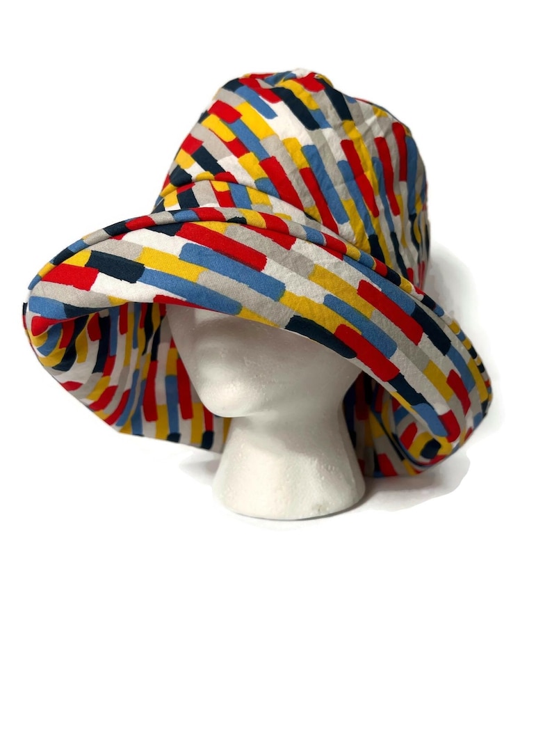 May include: A wide-brimmed bucket hat with a colorful geometric pattern. The hat is made of a soft, lightweight fabric and features a variety of colors, including red, yellow, blue, and gray.