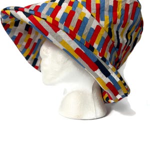 May include: A wide-brimmed sun hat with a colorful geometric pattern in shades of red, blue, yellow, and gray.