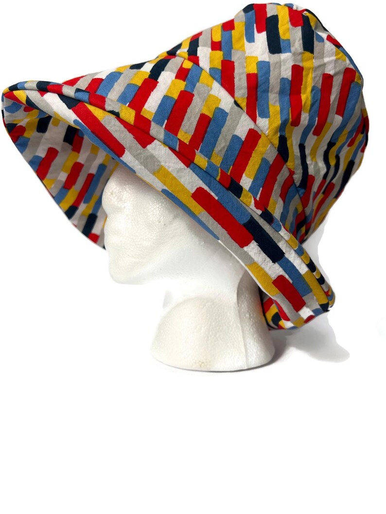May include: A wide-brimmed sun hat with a colorful geometric pattern in shades of red, blue, yellow, and gray.
