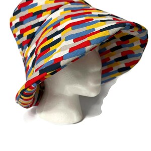 May include: A colorful bucket hat with a geometric pattern in shades of red, blue, yellow, and black. The hat is made of fabric and has a wide brim.