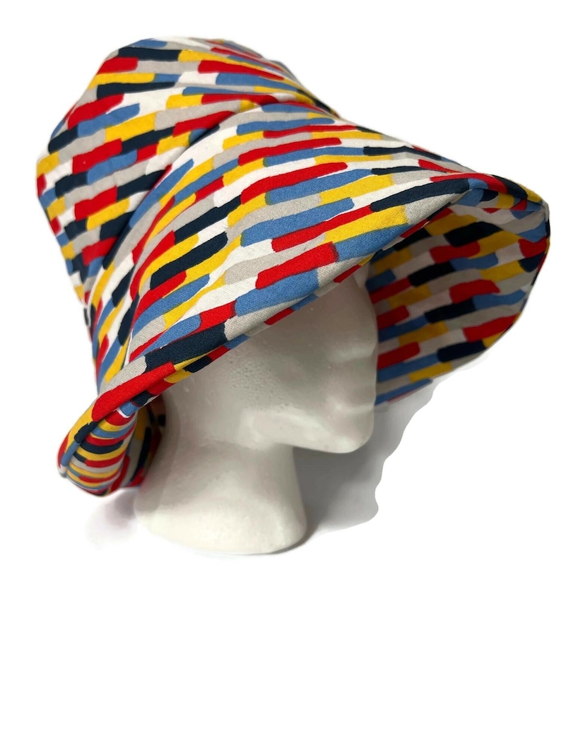 May include: A colorful bucket hat with a geometric pattern in shades of red, blue, yellow, and black. The hat is made of fabric and has a wide brim.