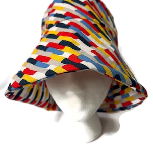 May include: A wide-brimmed bucket hat with a colorful geometric pattern in shades of red, yellow, blue, and gray.