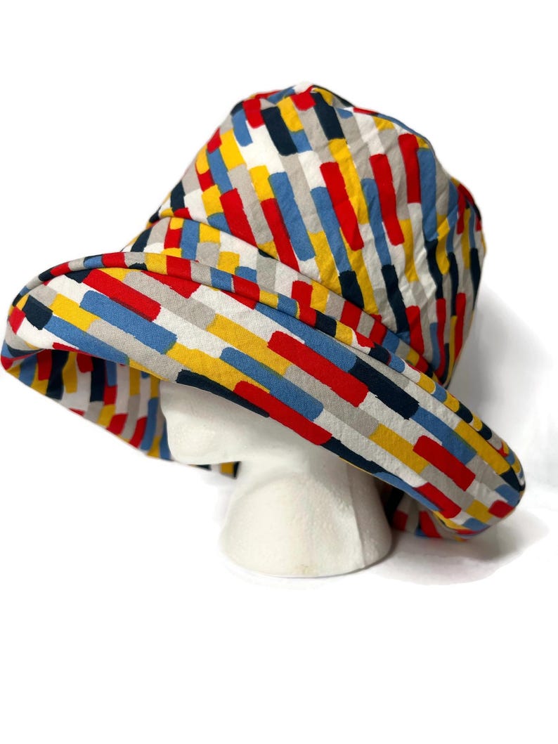 May include: A wide-brimmed hat with a colorful geometric pattern in shades of red, yellow, blue, and gray. The hat is made of a soft, textured fabric.