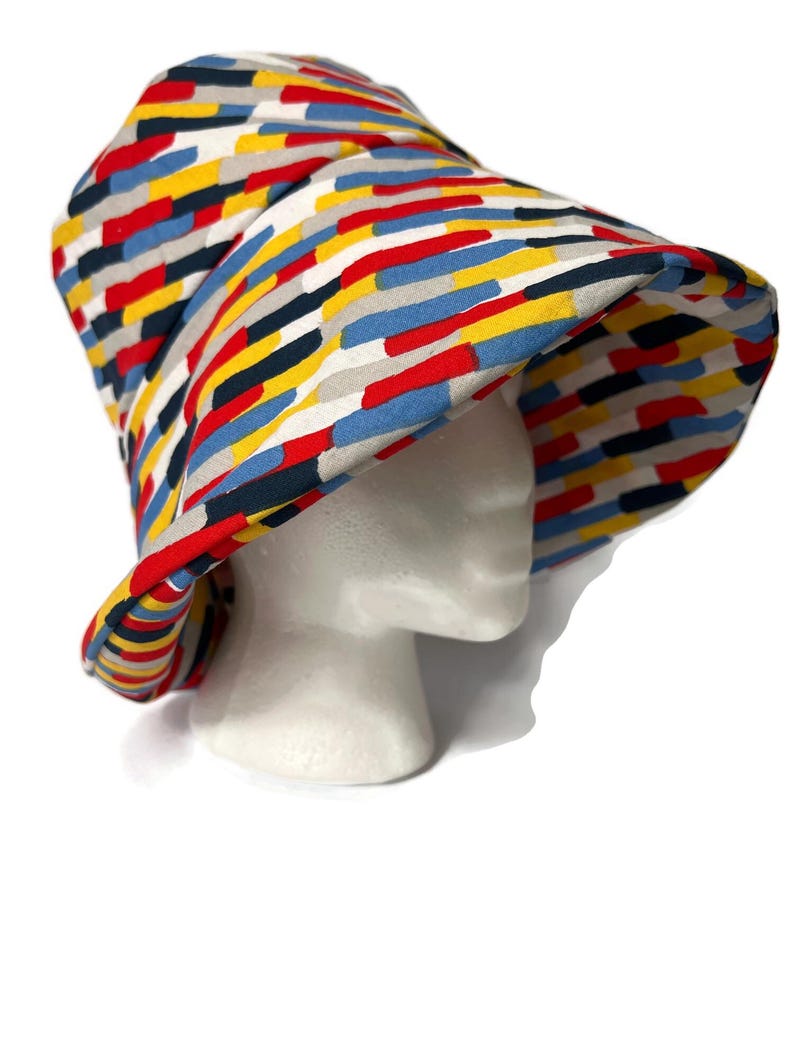 May include: A bucket hat with a colorful geometric pattern in shades of red, blue, yellow, and gray. The hat is made of fabric and has a wide brim.