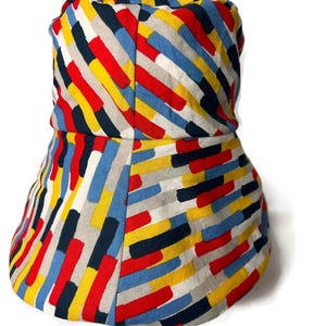 May include: A bucket hat with a colorful geometric pattern in shades of red, yellow, blue, black, and white. The pattern is made up of diagonal stripes of different widths.