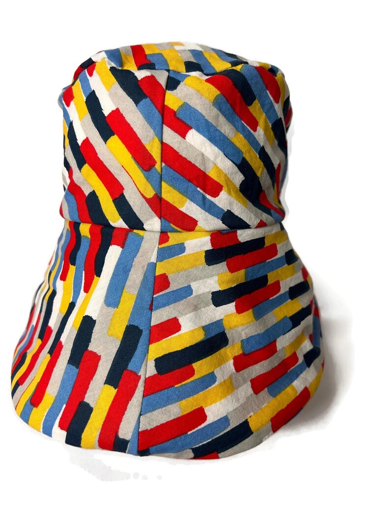 May include: A bucket hat with a colorful geometric pattern in shades of red, yellow, blue, black, and white. The pattern is made up of diagonal stripes of different widths.