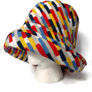 May include: A colorful bucket hat with a striped pattern in shades of red, yellow, blue, and black. The hat is made of a soft, lightweight fabric and has a wide brim.
