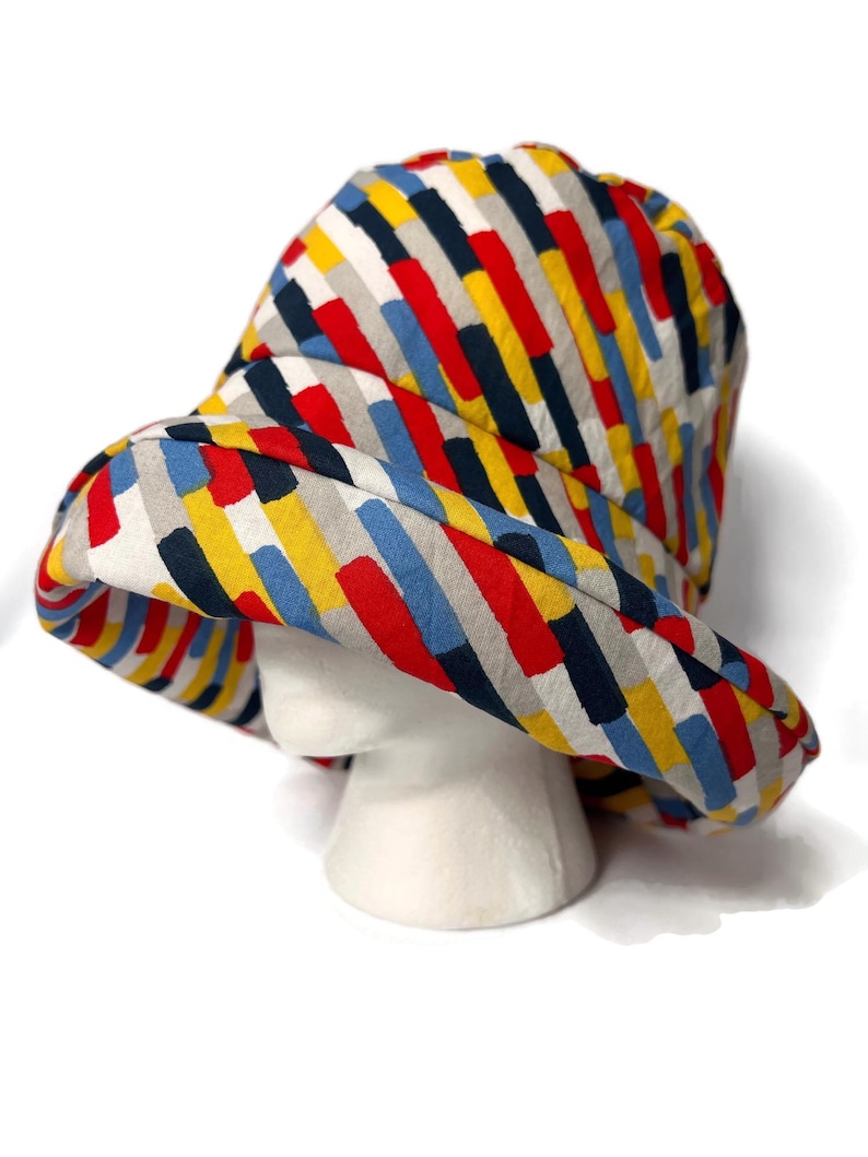 May include: A colorful bucket hat with a striped pattern in shades of red, yellow, blue, and black. The hat is made of a soft, lightweight fabric and has a wide brim.