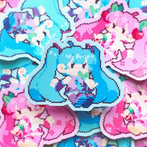 May include: A sticker with a pixelated cartoon character with long, light blue pigtails, wearing a purple outfit. The sticker has a light blue border and is surrounded by other similar stickers in shades of pink and blue.