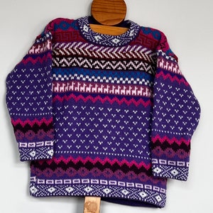 K&ouml;nnte beinhalten: Lila, rosa und wei&szlig; gemusterter Strickpullover mit Rundhalsausschnitt.