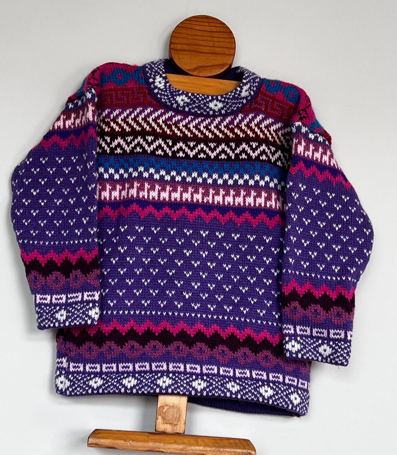 K&ouml;nnte beinhalten: Lila, rosa und wei&szlig; gemusterter Strickpullover mit Rundhalsausschnitt.