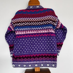 K&ouml;nnte beinhalten: Ein gestrickter Pullover mit hohem Kragen in einem Muster aus Lila, Rosa und Blau.