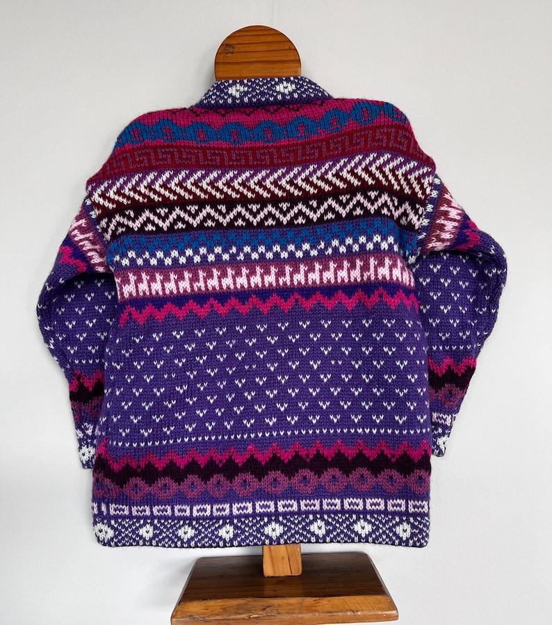 K&ouml;nnte beinhalten: Ein gestrickter Pullover mit hohem Kragen in einem Muster aus Lila, Rosa und Blau.