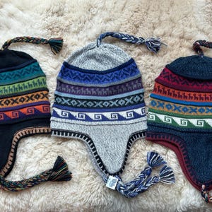 May include: Three knitted winter hats with ear flaps and colorful geometric patterns. The hats are in shades of blue, green, red, and orange.