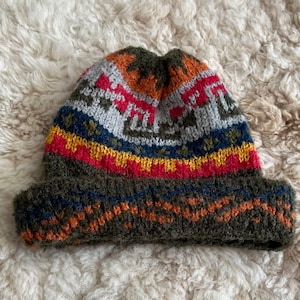 May include: A green knitted beanie with a colourful geometric pattern. The pattern includes red, yellow, blue, orange, and grey stripes.