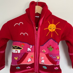 May include: Red knitted zip-up hooded sweater with colorful embroidered details. The design features a sun, birds, a house, and animals.