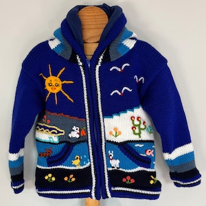 May include: Blue knitted zip-up jacket with a colorful embroidered design featuring a sun, birds, a cactus, and other animals. The jacket has a hood and two pockets.