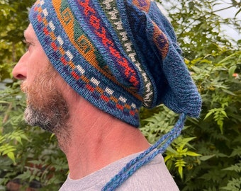 May include: A blue knit hat with a colorful geometric pattern. The hat has a slouchy fit and features a braided drawstring with wooden beads. The hat is a mix of blue, orange, green, and white.