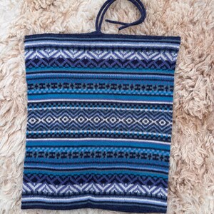 May include: A blue knitted tote bag with a geometric pattern in shades of blue, white, and black. The bag has a dark blue handle and is made of a soft, textured material. The bag is rectangular in shape.