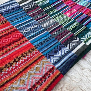 May include: A collection of colorful knitted textiles with geometric patterns. The textiles feature a variety of colors, including red, blue, green, and pink, with white and gray accents. The patterns include diamonds, zigzags, and stripes.