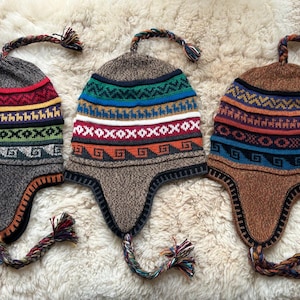 May include: Three knitted winter hats with ear flaps and long tassels. The hats feature colourful geometric patterns and are made of a soft, warm material.